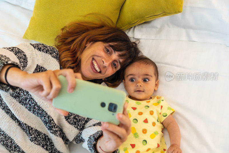 一位年轻的白人母亲和她可爱的宝宝在床上自拍的俯视图