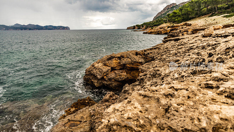 地中海的风景，在巴利阿里群岛的阿尔库迪亚。西班牙，西班牙的风景。美丽的自然和高山岩石。天空中乌云密布。周围有森林和沙滩