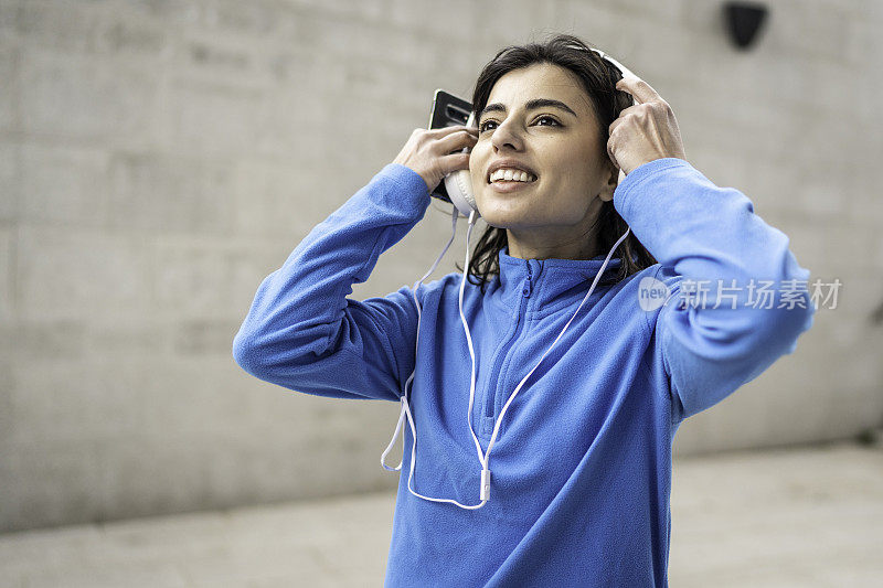 年轻快乐的运动女子在城市背景听音乐