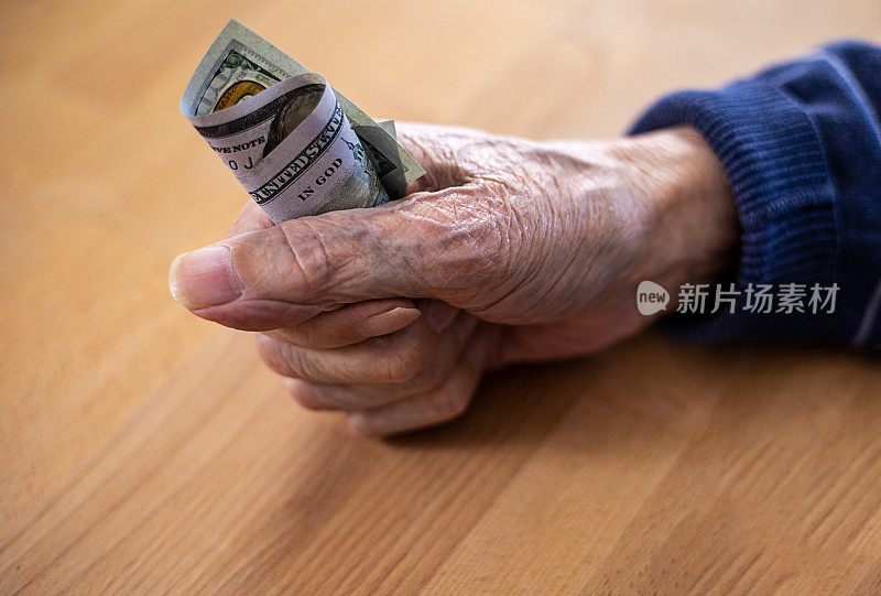 一位老人握紧拳头，手里握着一张钞票