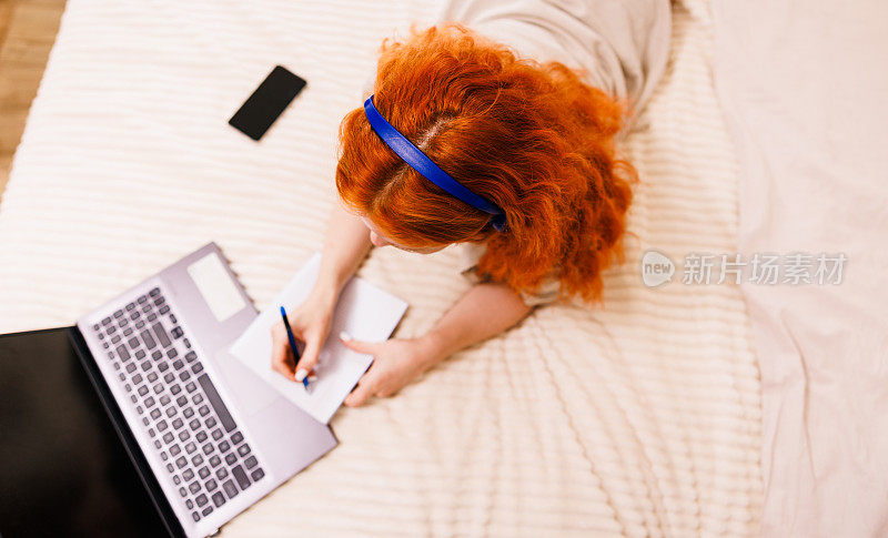 卷发女孩躺在沙发上，看着电脑屏幕笔记本电脑。空白的白屏幕。模拟。视频会议，工作或在家在线学习。