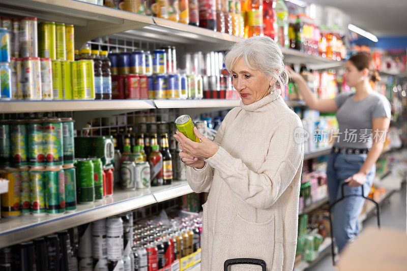 一位老妇人在超市的食品杂货区挑选装在铝罐里的碳酸饮料