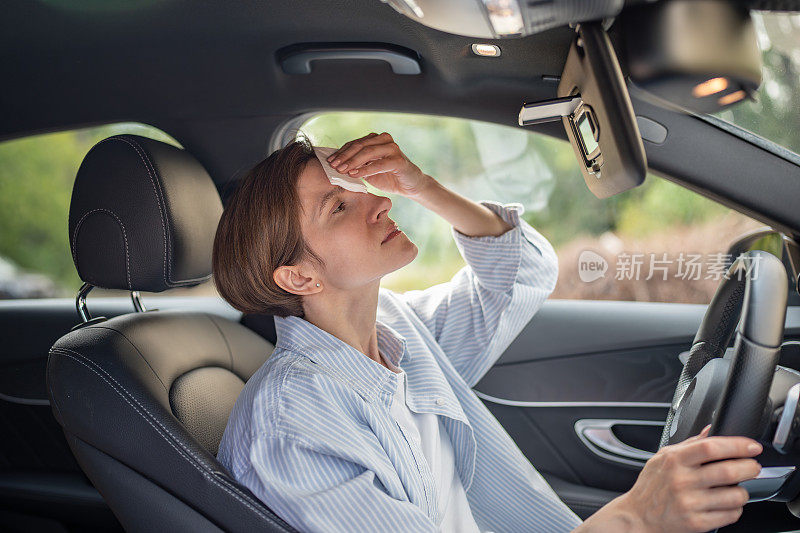 女子在炎热的夏天开着空调坏了的车擦汗纸巾。