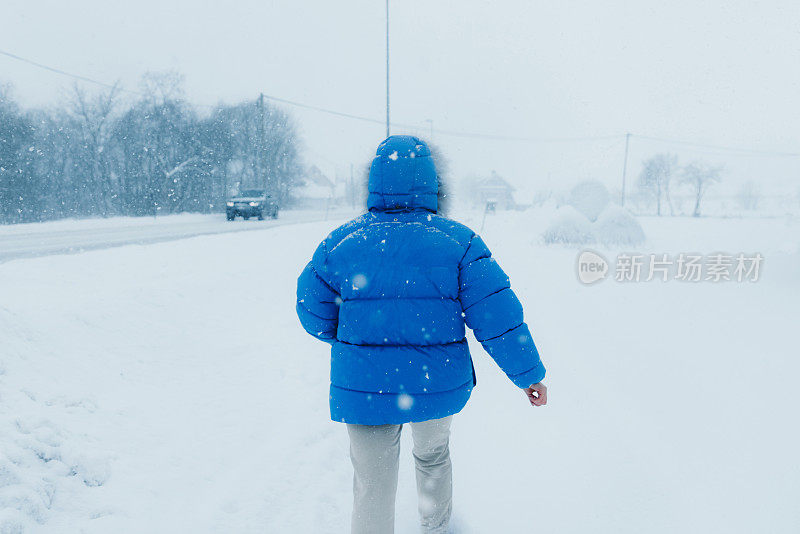 一名穿着蓝色外套的女子在大雪中漫步在斯堪的纳维亚村庄的街道上，欣赏冬天