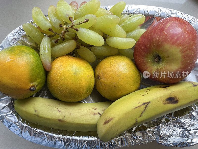 全画幅的锡箔衬里的水果碗包含三个橙子，两个香蕉，一串白葡萄和红苹果，高架视图