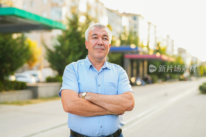 白发中年男子双手交叉在户外的画像