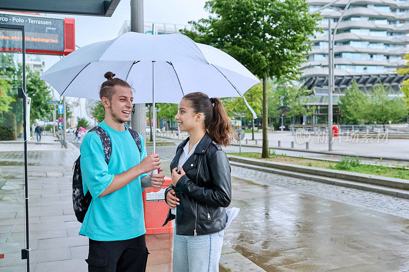 十几岁的男孩和女孩在公共汽车站撑着伞等公交车