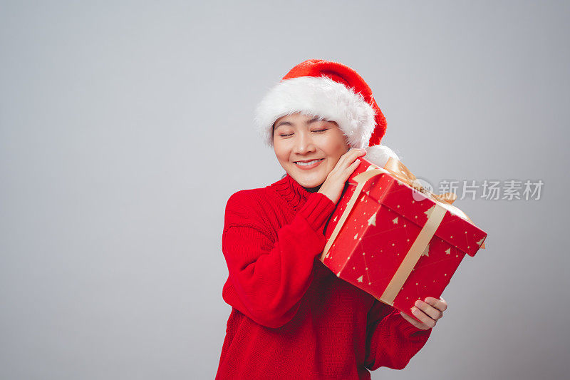亚洲女人戴着圣诞老人的帽子，拿着礼盒开心地微笑，孤立在白色的背景上。