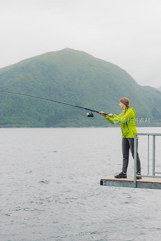 身穿绿夹克的女子在挪威峡湾钓鱼