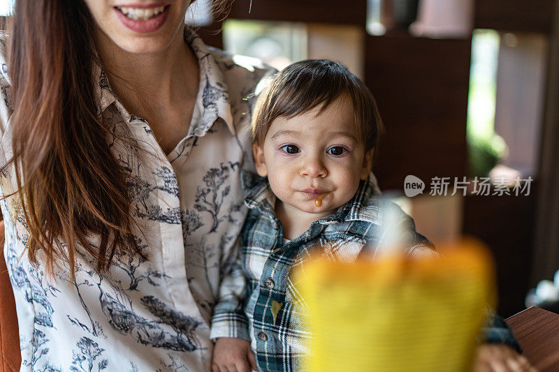 母亲抱着吃着塑料包装水果泥的可爱男婴，