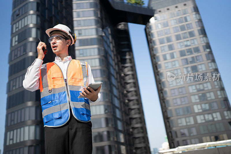 肖像亚洲的男工程师穿着防护工作服，正在屋顶大楼用平板电脑和对讲机进行系统检查
