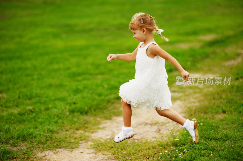 侧面的微笑女孩在白色的裙子在公园里跑步