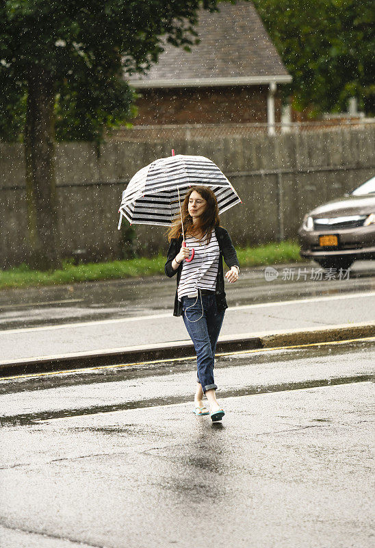 少女撑着伞在雨中走在街上。纽约皇后区