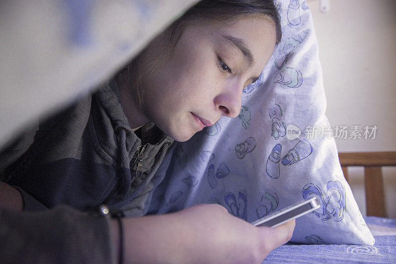 青少年白天躺在毯子下使用智能手机