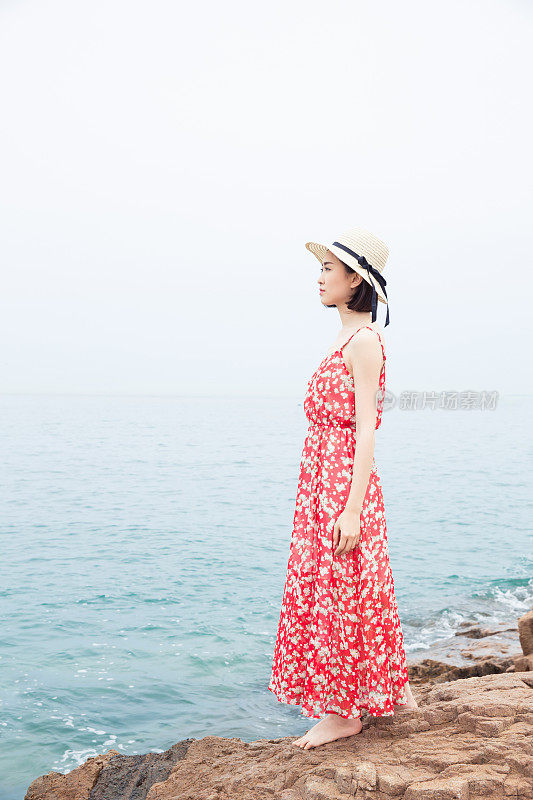 美丽的女人站在岩石上，蓝色的大海为背景