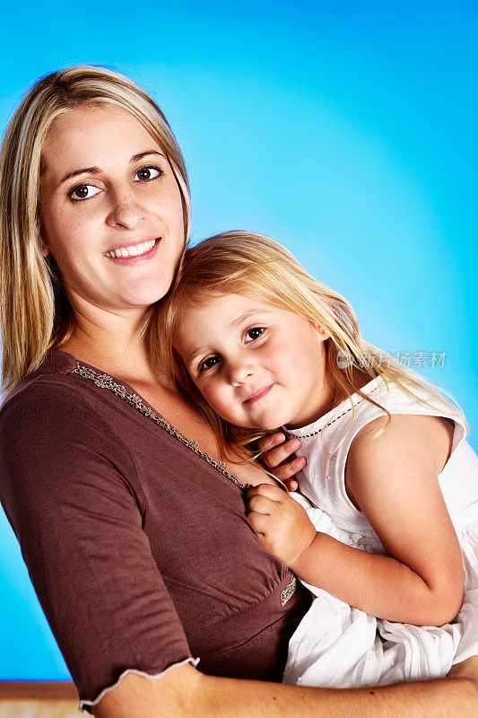 美丽的金发母亲抱着可爱的蹒跚学步的女儿和微笑