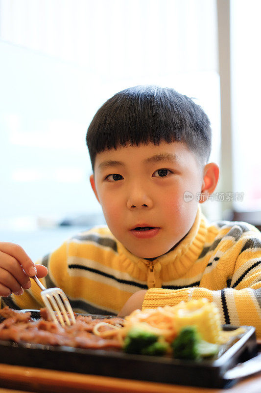 亚洲男孩在餐厅吃牛排