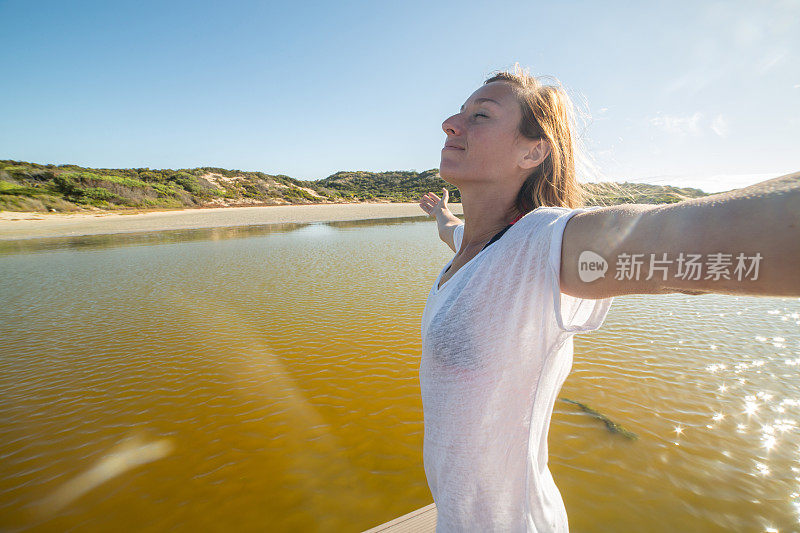 年轻女子在湖上的防波堤上张开双臂