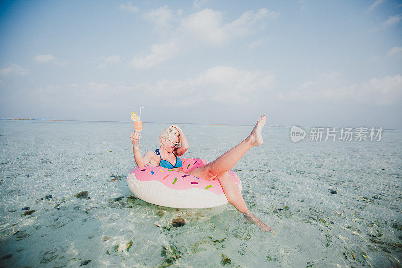 性感的女人浮在水上，有鸡尾酒时间在海洋，马尔代夫