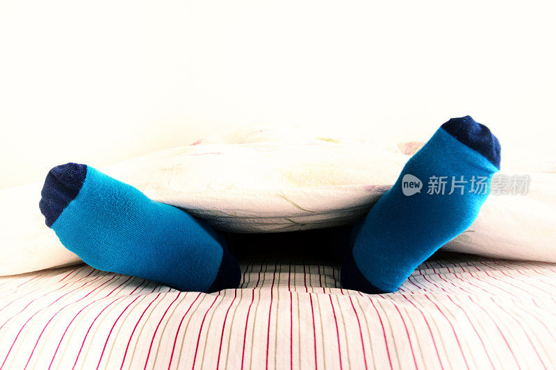 睡在彩色袜子:男人的脚从羽绒被伸出