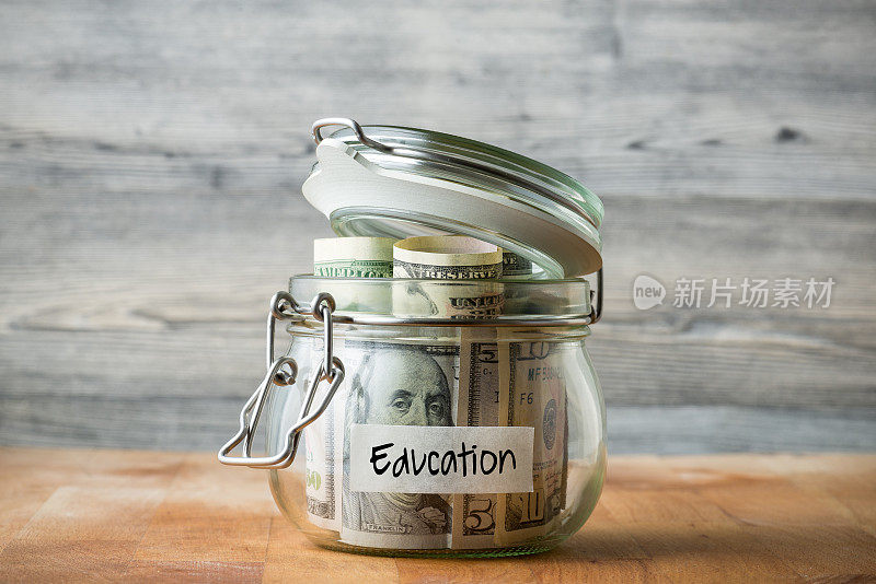 在木制背景上孤立的玻璃罐中的美元。为教育存钱。