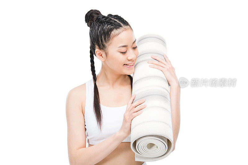 快乐迷人的亚洲女孩在运动服装与辫子持有瑜伽垫孤立的白色
