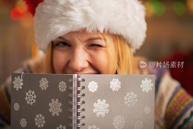 戴着圣诞帽的少女躲在记事本后面眨眼
