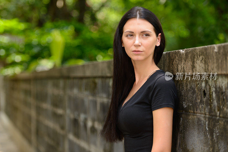 年轻美丽的女人靠在街上的旧混凝土墙上