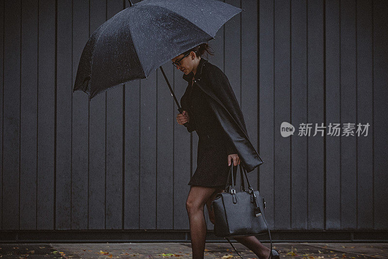 一名年轻女子撑着伞，在寒冷的秋日里在风雨中行走。