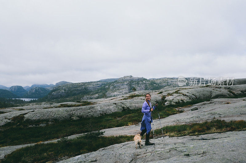 妇女和狗徒步旅行到布道石在挪威