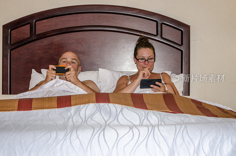 一对异性夫妇在床上并排使用手机
