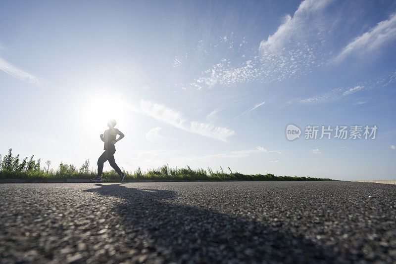 年轻的男运动员在柏油路上迎着天空奔跑