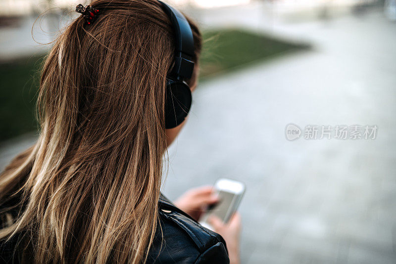 一个女孩在户外戴着耳机听音乐的后视图。