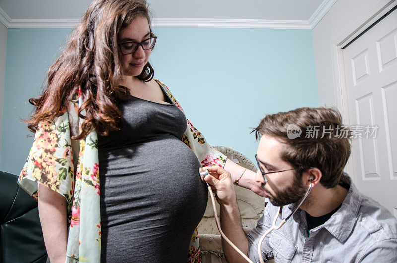 年轻男子用听诊器在他怀孕女友的肚子上听婴儿的声音