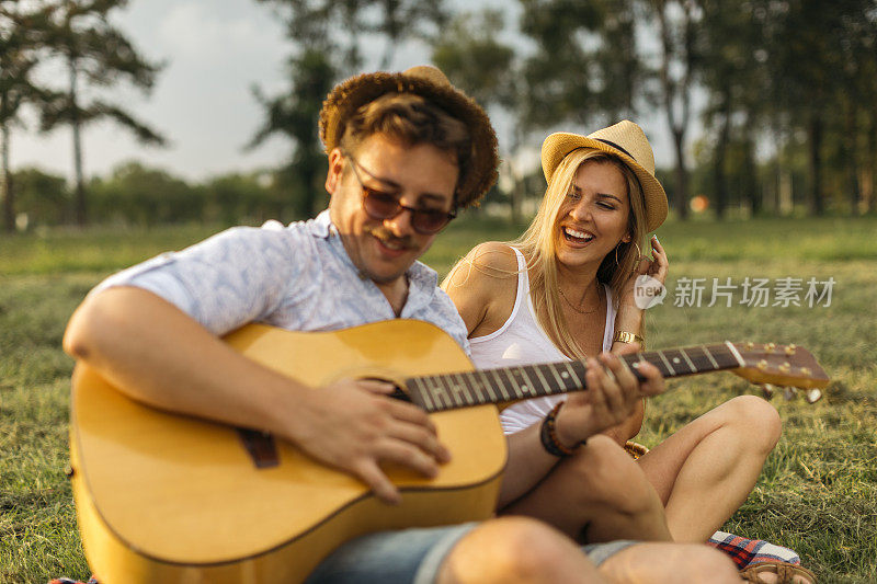 一对年轻情侣坐在草地上，手里拿着吉他