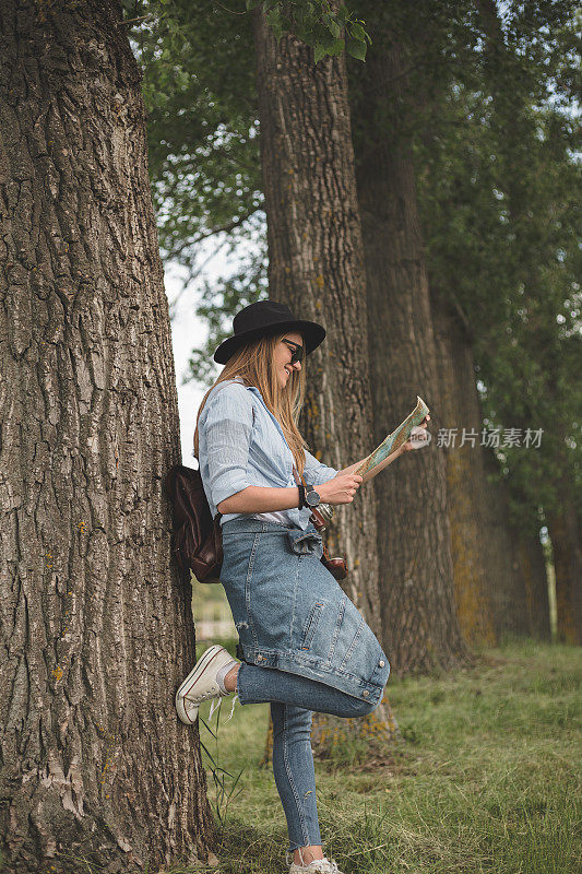 可爱的女人一边靠在树上一边看地图