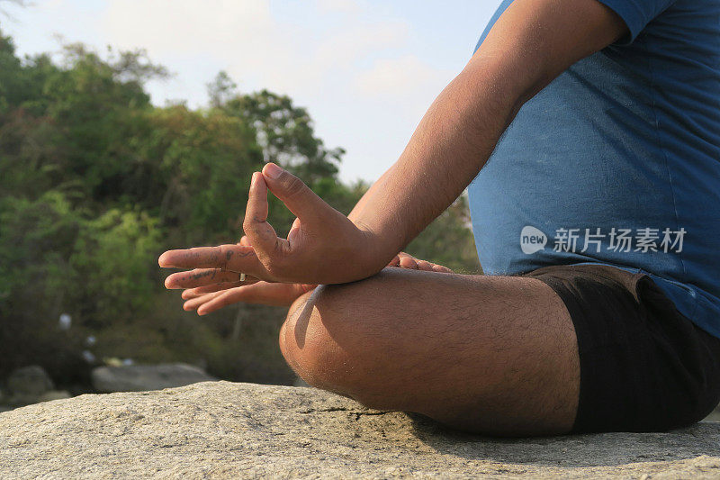 近距离的侧面图像，印度男子的手，同时练习莲花姿势(莲花瑜伽)瑜伽位置上的岩石，帕洛伦海滩，果阿，印度