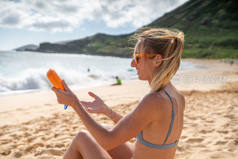 夏日――年轻女子在海滩上涂抹防晒霜，保护皮肤