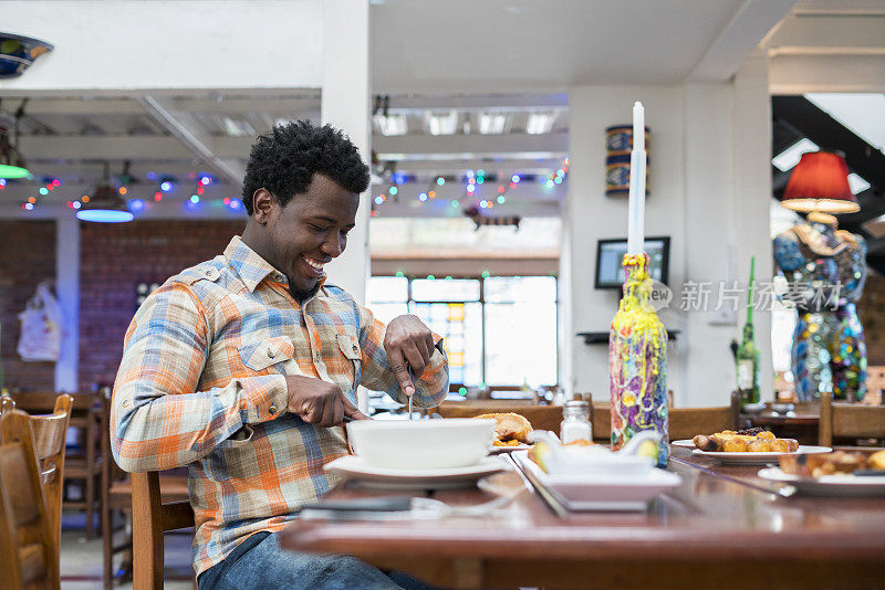 一个大约29岁的拉丁男子，深色皮肤，非洲式头发，正坐在一个美丽的餐馆的木桌上，典型的哥伦比亚食物吃着他的美味的最喜欢的菜，他的脸上有一个大sorisa