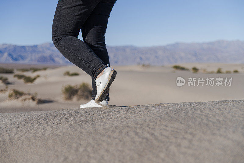 在加州死亡谷梅斯奎特平原的沙丘上徒步旅行的妇女。注意腿，特写。