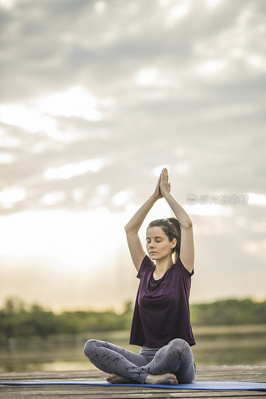 女子练习瑜伽，而坐在莲花位置在湖码头