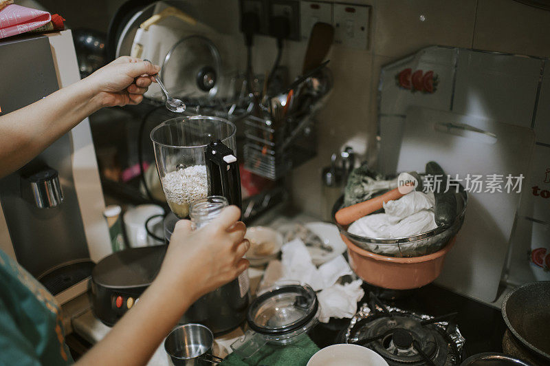 一名亚裔华人女性在厨房用电子搅拌机和其他厨房用具做饭准备早餐