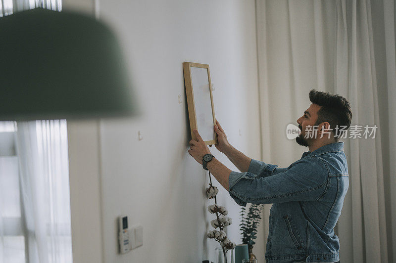 一个留着胡子的中东男人在客厅的墙上挂着一幅画