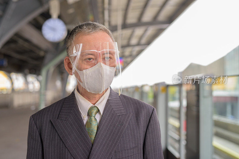 成熟的日本商人戴着面具和面罩在轻轨站等候