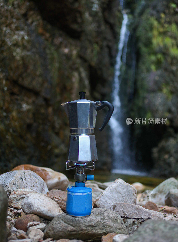 野营煤气炉上的咖啡壶，背景是瀑布。