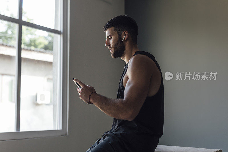运动员穿着运动服，在健身房使用智能手机和无线耳机