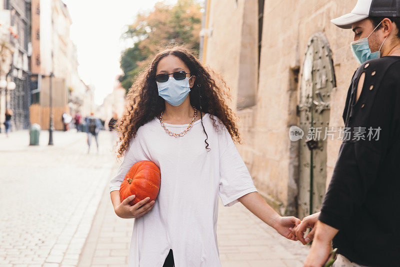 一名年轻女子和一名戴着防护面具的男子学生在秋天的周末带着南瓜走在老街上