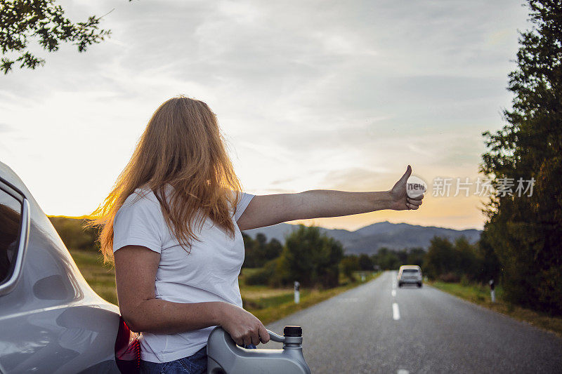 一位妇女在路上试图修理一辆坏了的汽车。这位妇女给她的车加油，试图继续旅程。一个女人带着一桶汽油在一辆车旁边