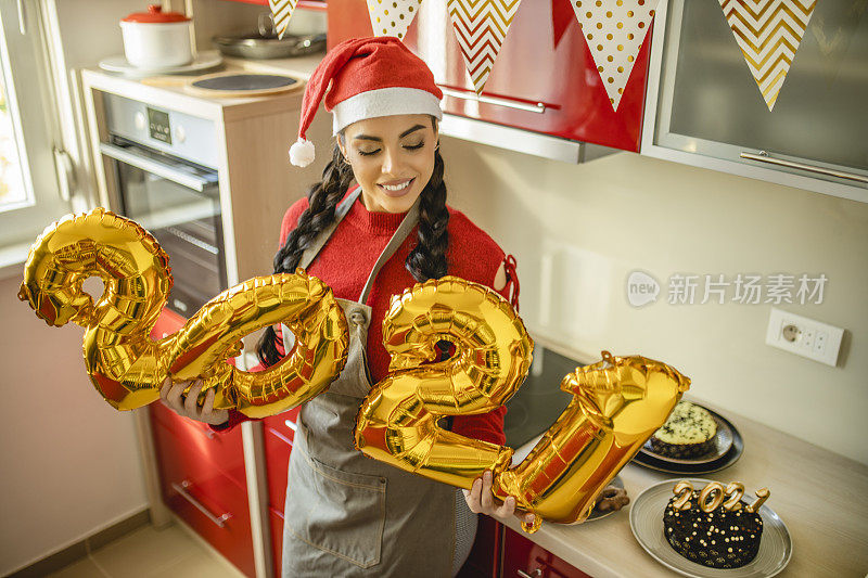 一名女子在家里开心地庆祝新年，她拿着巨大的金色气球，形状是数字2021，代表即将到来的新年