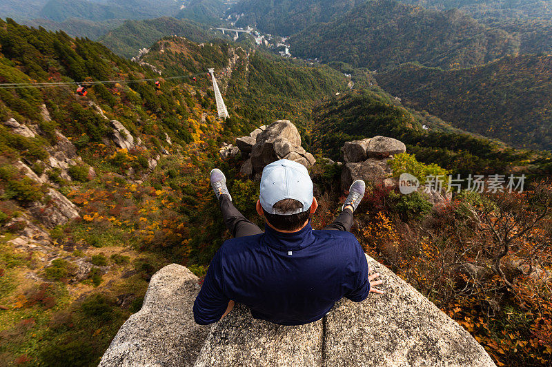 一名男子坐在悬崖边上的山上的秋天山戈寨索